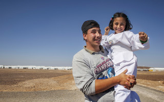 Munaf, 21, holds up his sister Solaf, 9, as she demonstrates her new taekwondo skills at Azraq refugee camp in Jordan. © UNHCR / A. SAKKAB
