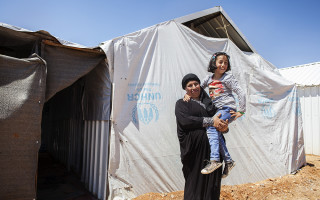 Ruwaidah, 44, holds her energetic daughter Solaf, 9, in front of their container at Azraq refugee camp. “She’s always on the move, never stays in one place.” © UNHCR / A. SAKKAB