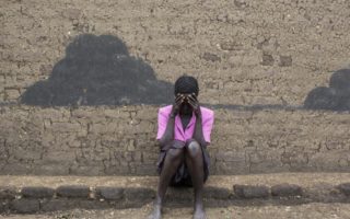 Refugee from South Sudan sits on a curb against a wall with her head in her hands in Uganda
