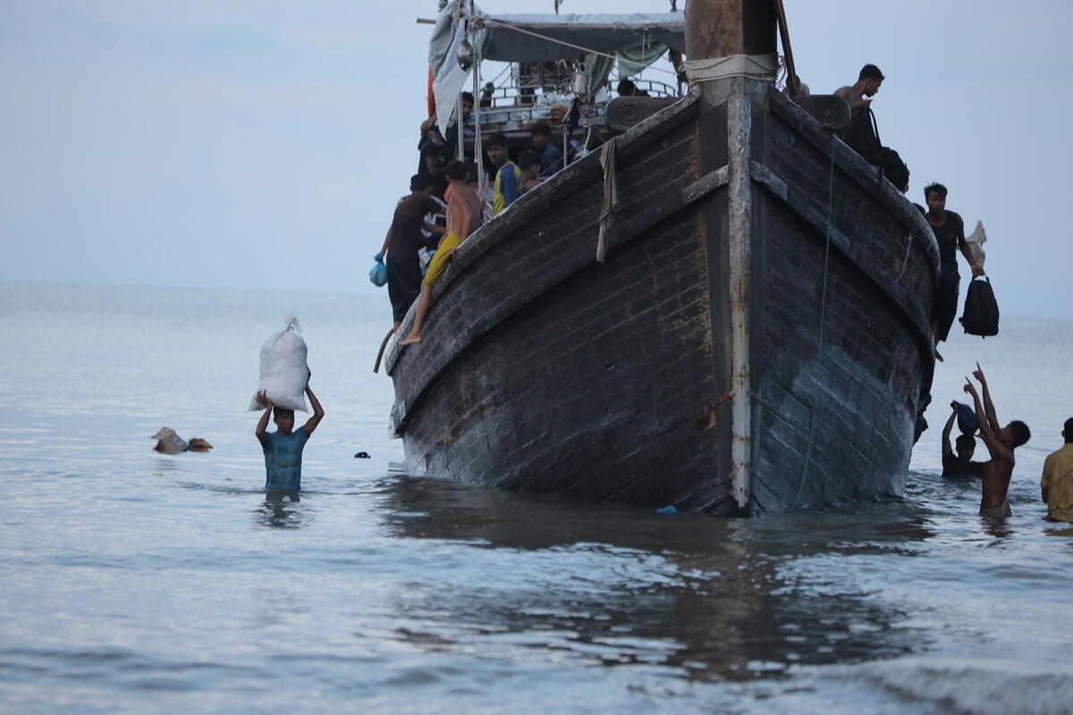 Bateau au milieu de la mer avec un ciel bleu. Des personnes sur le bateau déchargent des sacs à d'autres sont dans l'eau.