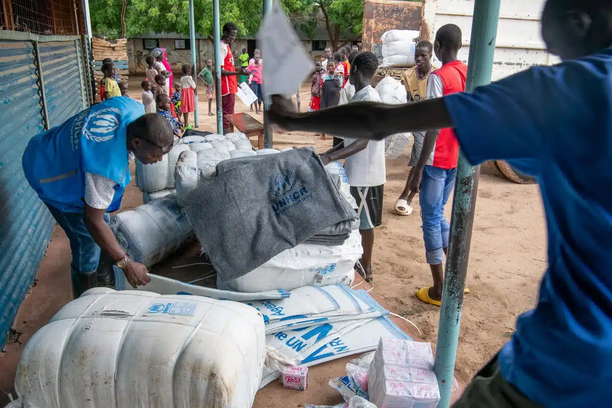 Un homme vêtu d'un gilet bleu du HCR se penche sur une pile de produits humanitaires de la marque du HCR.
