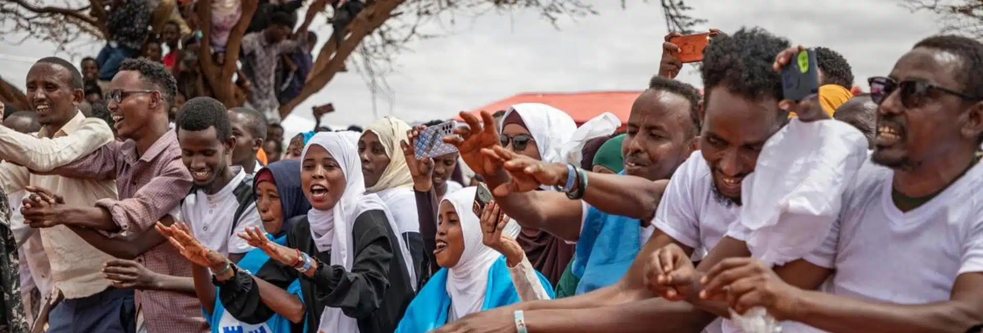 A joyous crowd wearing colourful clothing is smiling and gathered outside.