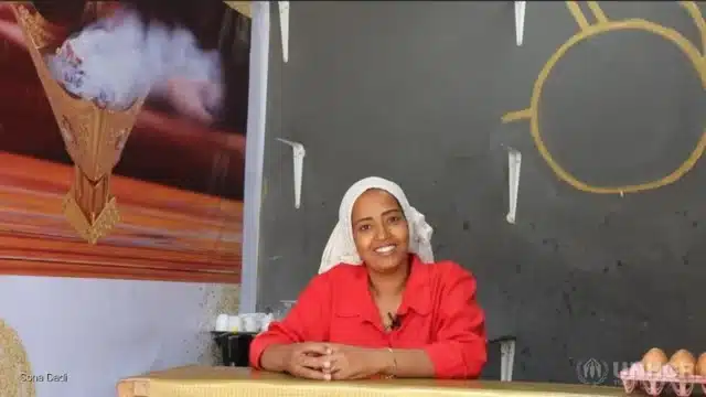 Woman smiling, sitting behind a counter inside a shop.