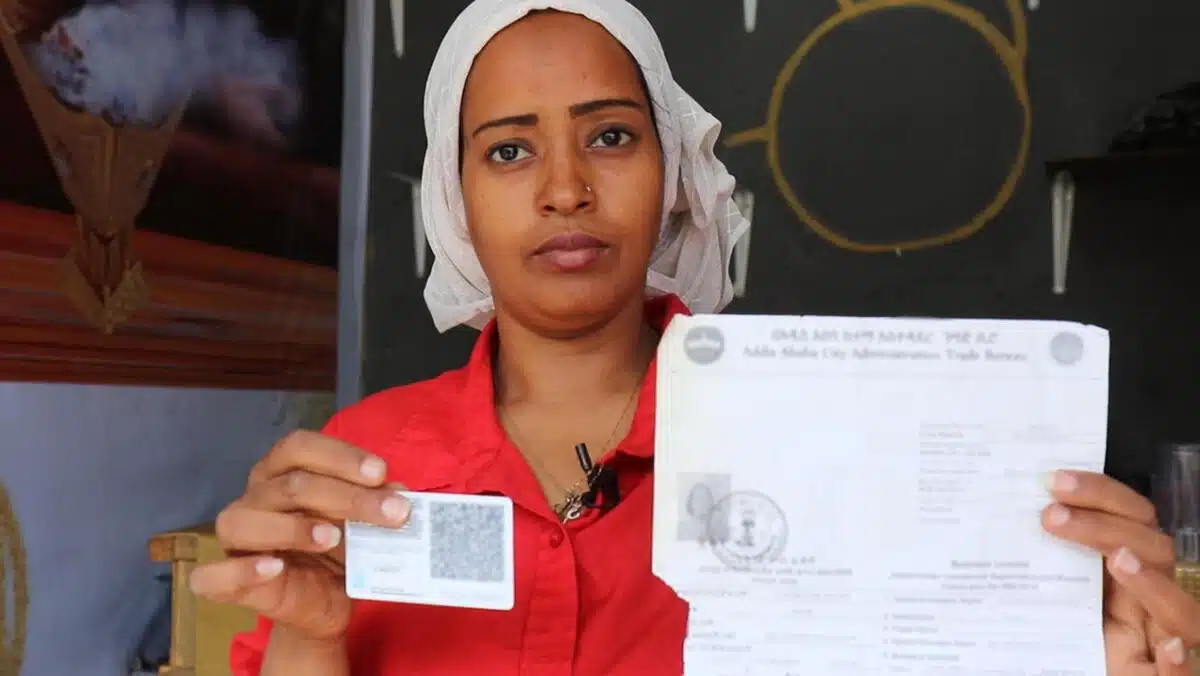 Woman staring into the camera, holding up two pieces of paper.