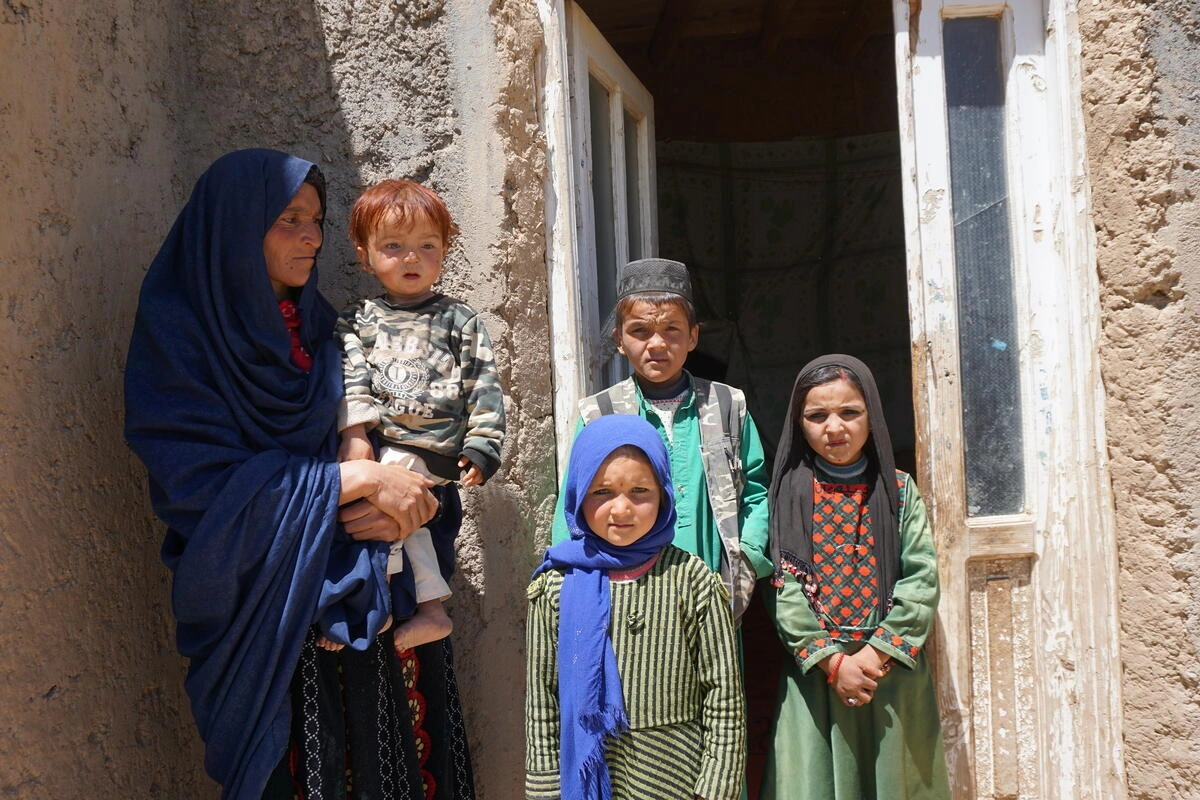 Woman holding a child as she stands next to 3 other children. Behind them is an entrance to a house.