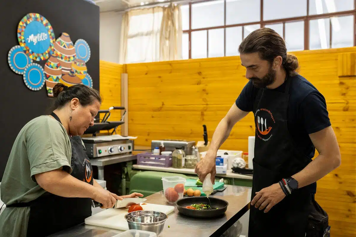 Two people are in a kitchen cooking together. One is sitting and the other one is standing.