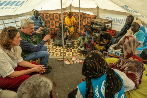 Group of people sitting in a circle inside a UNHCR tent.