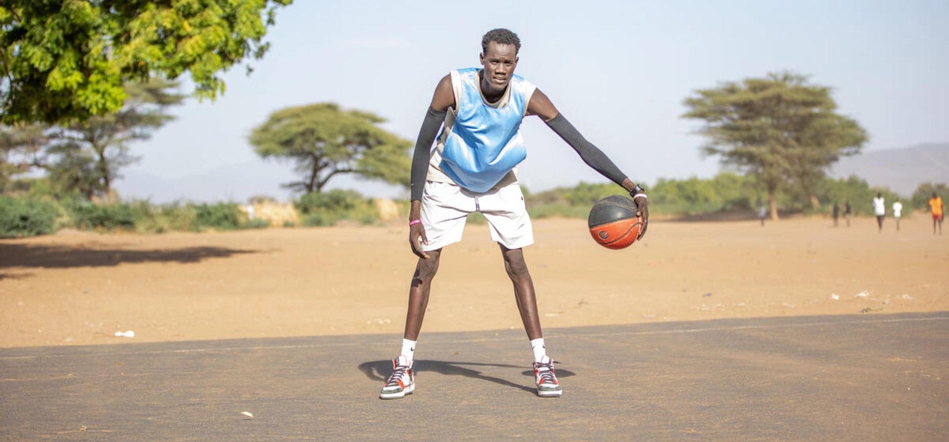 A man wearing sports clothes is playing with a basketball. He is in a sand-filled area.
