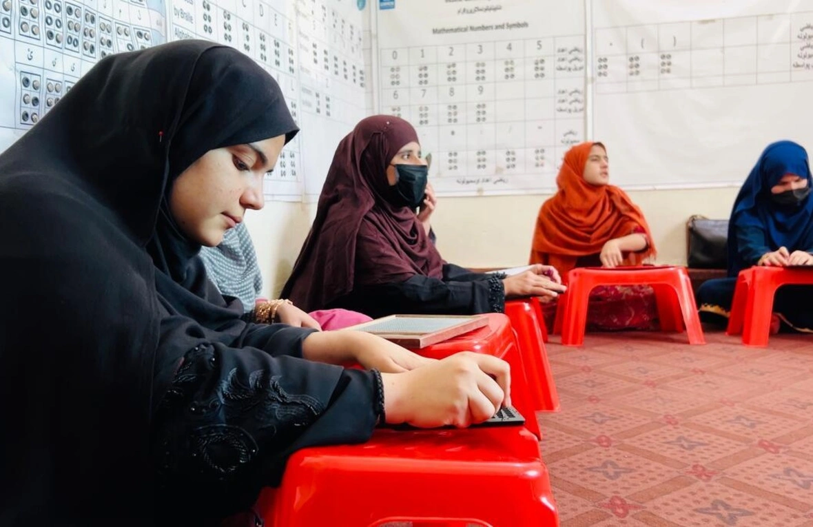 A group of women are sitting on the ground. They seem to be in a learning session. They are also also wearing headscarves.