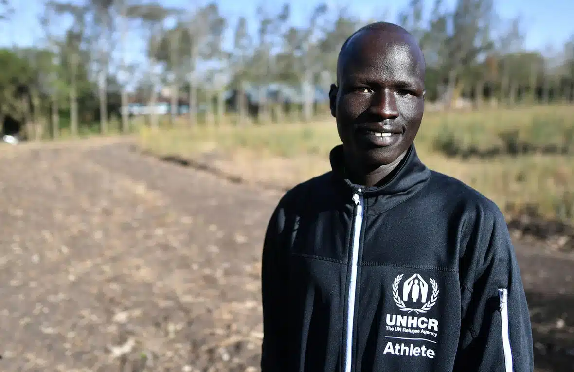 A man wearing a black UNHCR-labelled jacket is standing in a remote location.