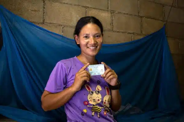 Woman in purple shirt with a cartoon bunny on it standings in front of a blue fabric backdrop. She is holding an ID card.