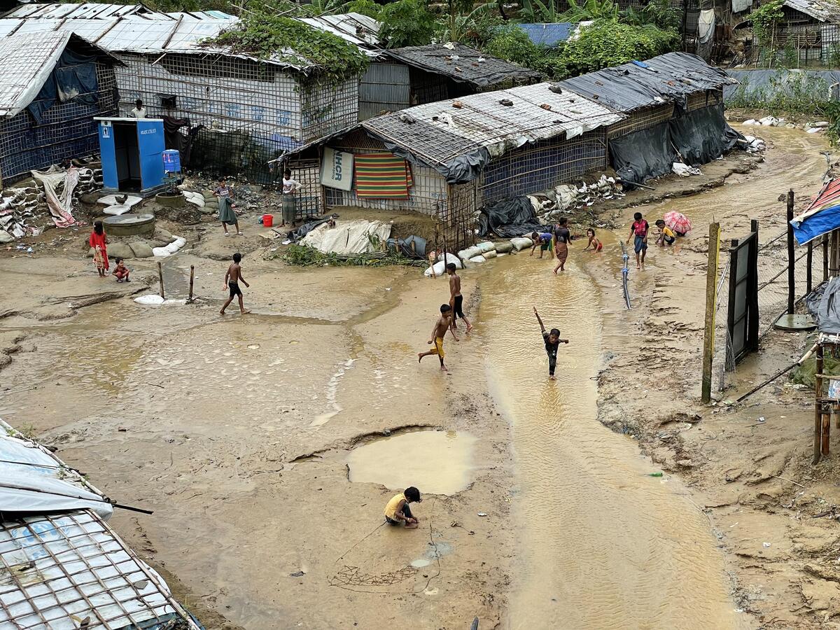 Children can be seen playing in a muddy street lined with temporary shelters for refugees.