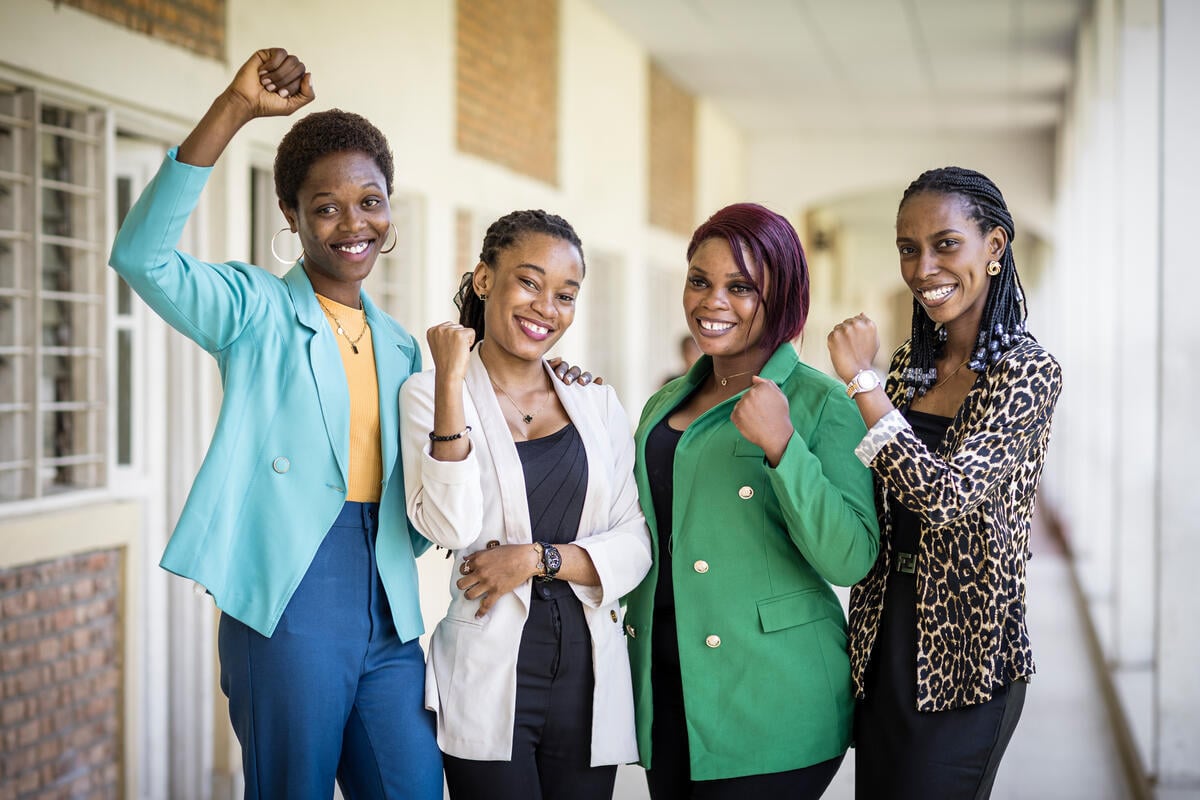 Four young black women  stand in a hallway and pump their fists smiling to the camera.