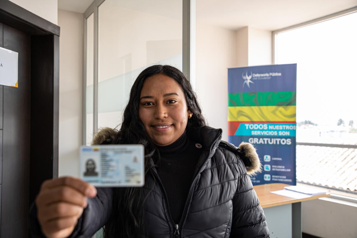 Une Vénézuélienne souriante aux longs cheveux noirs, vêtue d'un manteau noir, tient à la main une nouvelle carte d'identité.