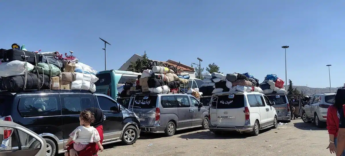 Plusieurs camionnettes s'entassent sur un chemin de terre avec des bagages empilés sur les véhicules. Ils se dirigent tous dans la même direction.