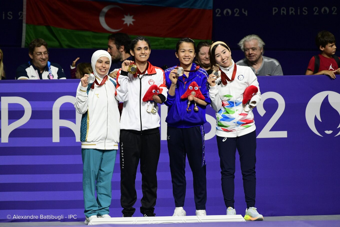 Les athlètes paralympiques exhibent fièrement leurs médailles devant le drapeau de l'Azerbaïdjan et une foule bloquée par un mur portant l'inscription «Paris 2024»