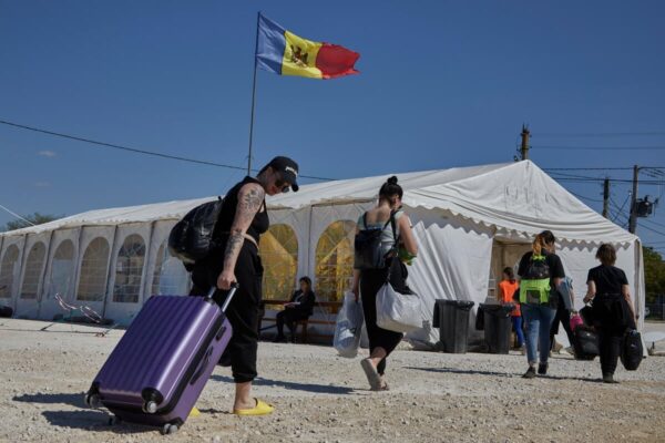 Des personnes transportent des bagages et des affaires sur un trottoir rocailleux en direction d'une tente blanche surmontée du drapeau de la République de Moldavie.