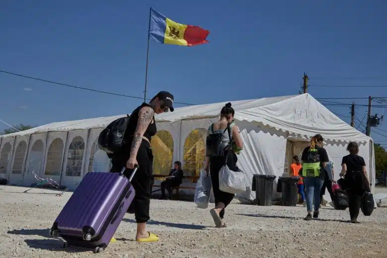 People carry luggage and belongings on rocky pavevment towards a white tent with the Republic of Moldova's flag on top.