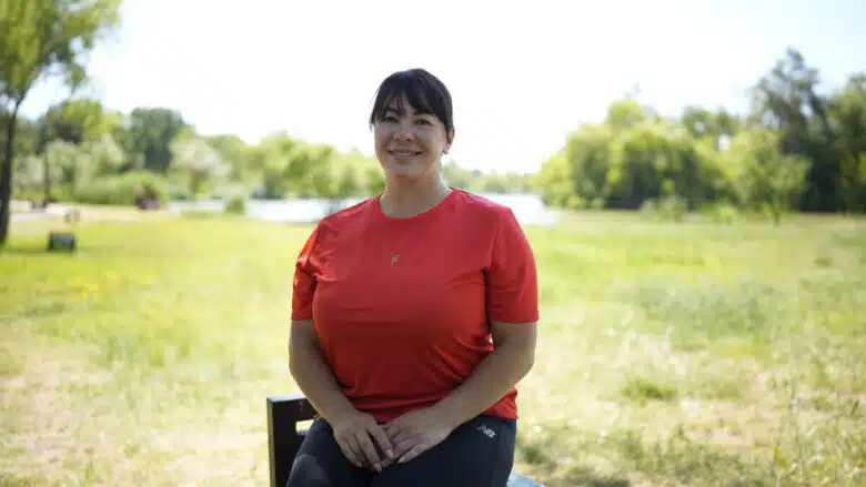 Woman wearing a red shirt sits to pose for a photo outdoors.