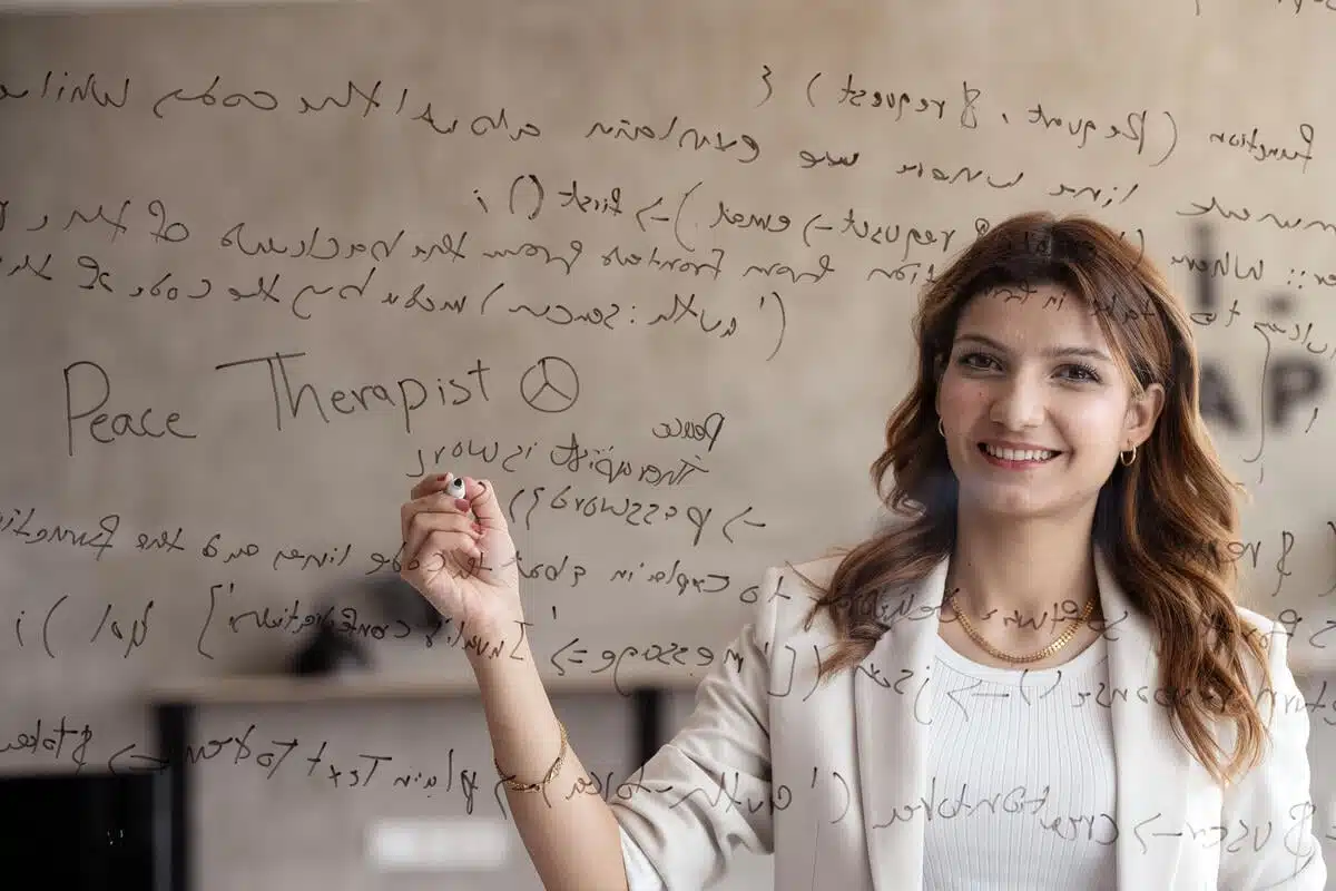 Woman writes a wesbite code into a mirror. She is wearing a tan blazer and a white shirt.