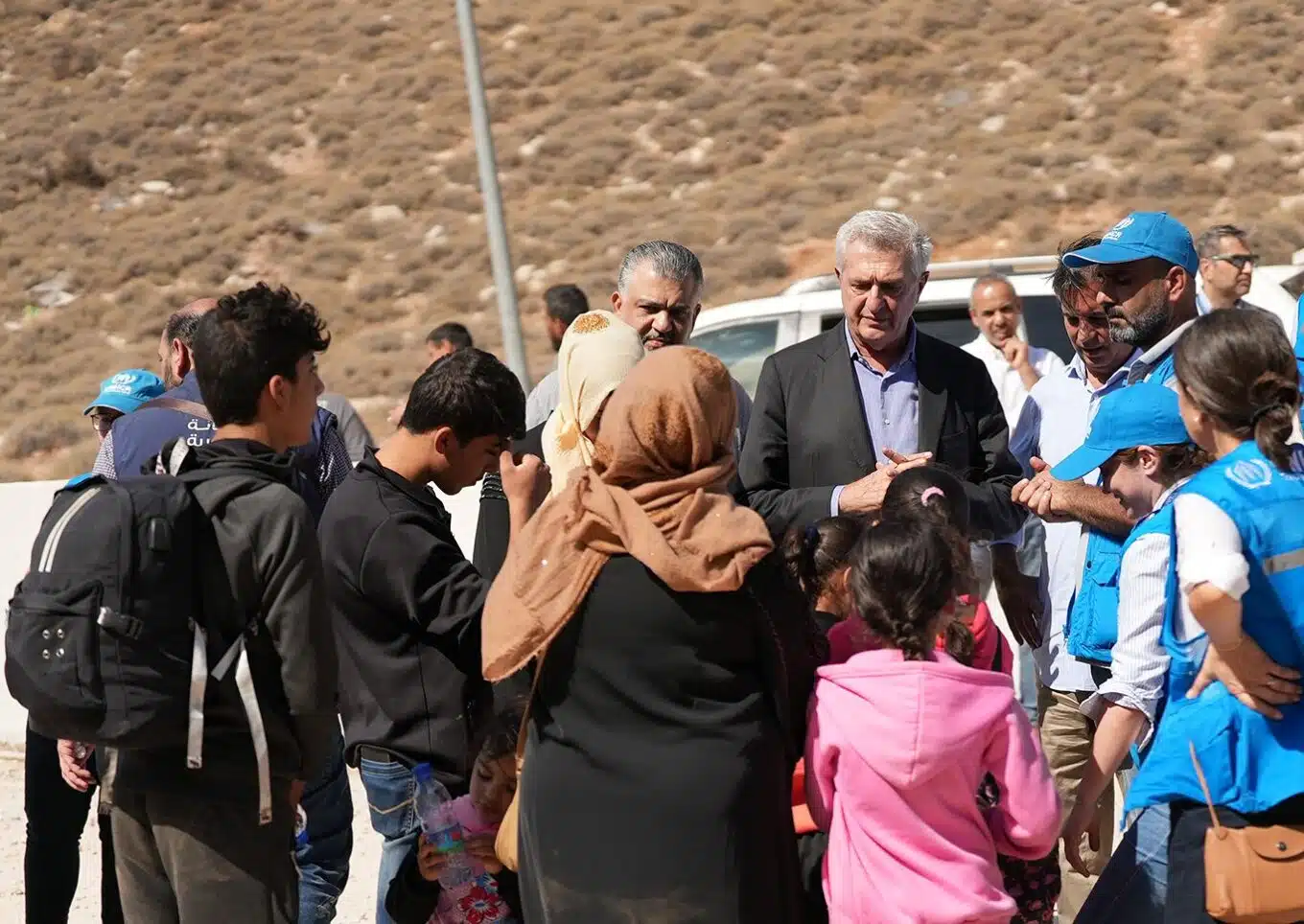 Several people wearing UNHRC vests and two men in formal attire stand in front of a family.