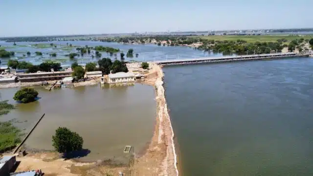 A river flows in between a village. The village lands are now filled with water, houses are just barely above the water line.