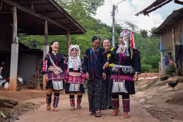 Five people in cuktural dress walk along a dirt path while smiling, laughing and chatting with one another.