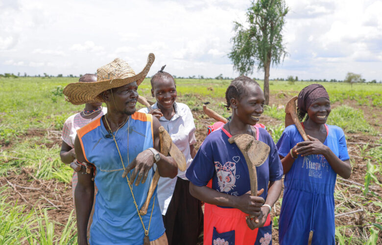 Cinq personnes sourient vers la droite de l'écran en tenant des outils agricoles.