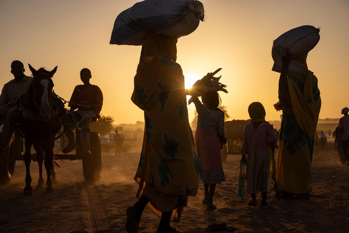 Silhouettes of a group of Sudanese refugees carrying their belongings over their heads can be seen over a setting sun in the desert.