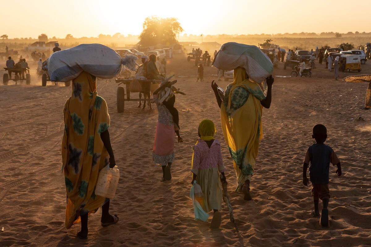 La caméra se concentre sur cinq personnes, deux adultes et trois enfants. Leurs dos sont tournés vers la caméra, tandis que les provisions sont transportées dans la direction du soleil. La zone est encore plus sombre que.