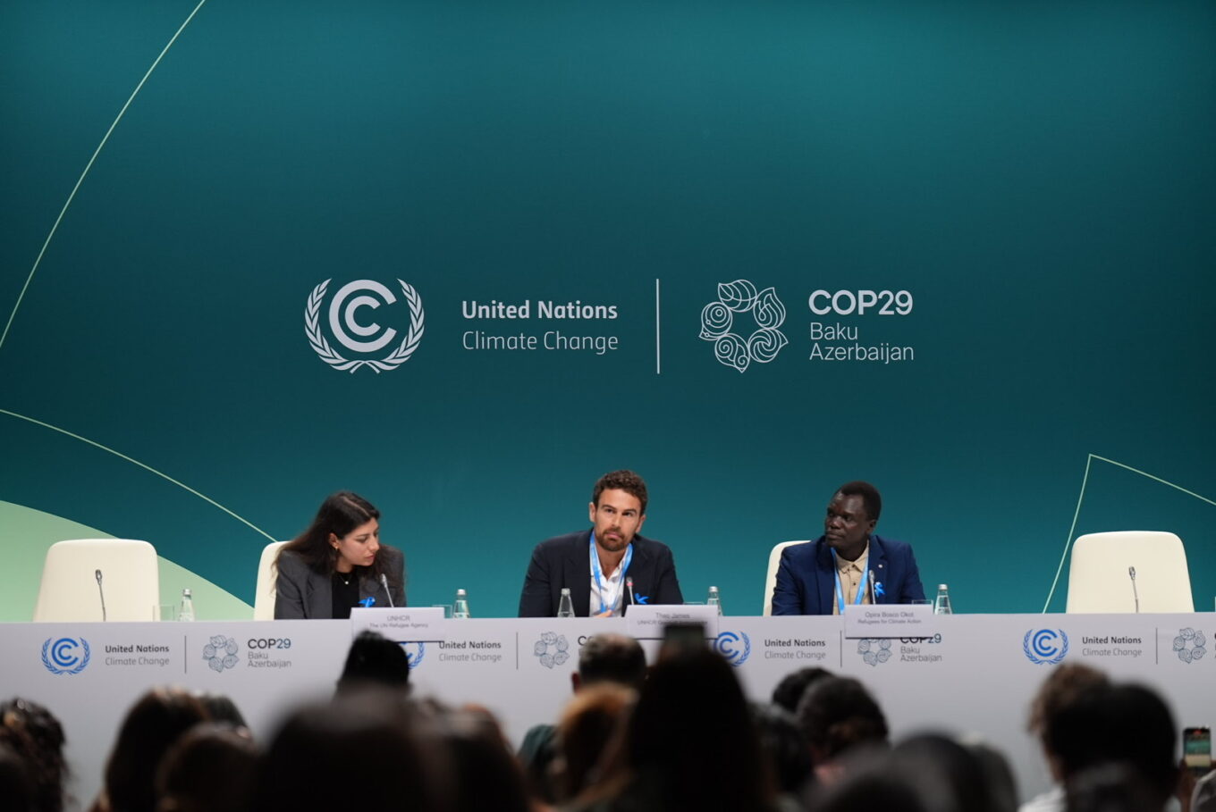 Trois personnes sont assises sur un panneau devant un groupe de fond vert émeraude qui affiche le logo des Nations unies sur le changement climatique et de la COP29.