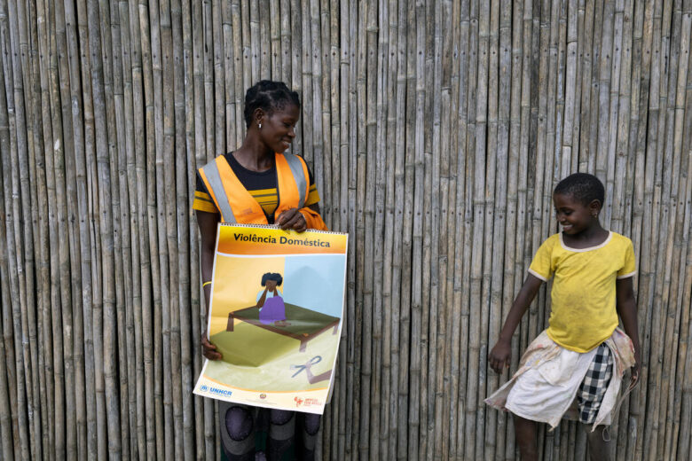 A woman holds a sign about domestic violence while smiling at a girl beside her. Both are smiling, and behind them is a bamboo wall.