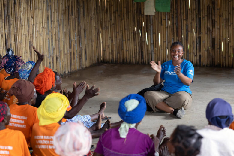 A woman seated on the floor claps along with a group of people in a community center.