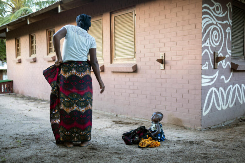 A woman adjusts her capulana which is a traditional piece of cloth often worn as a skirt while her six-month old baby girl looks on