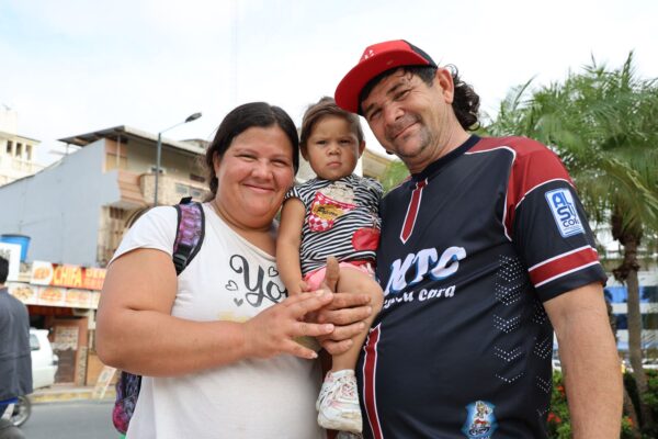 A smiling woman and a man holding their infant daughter pose for a photo on a street in Ecuador.