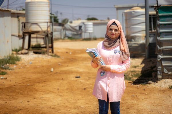 A woman dressed in pink stands in front of a camera holding books.